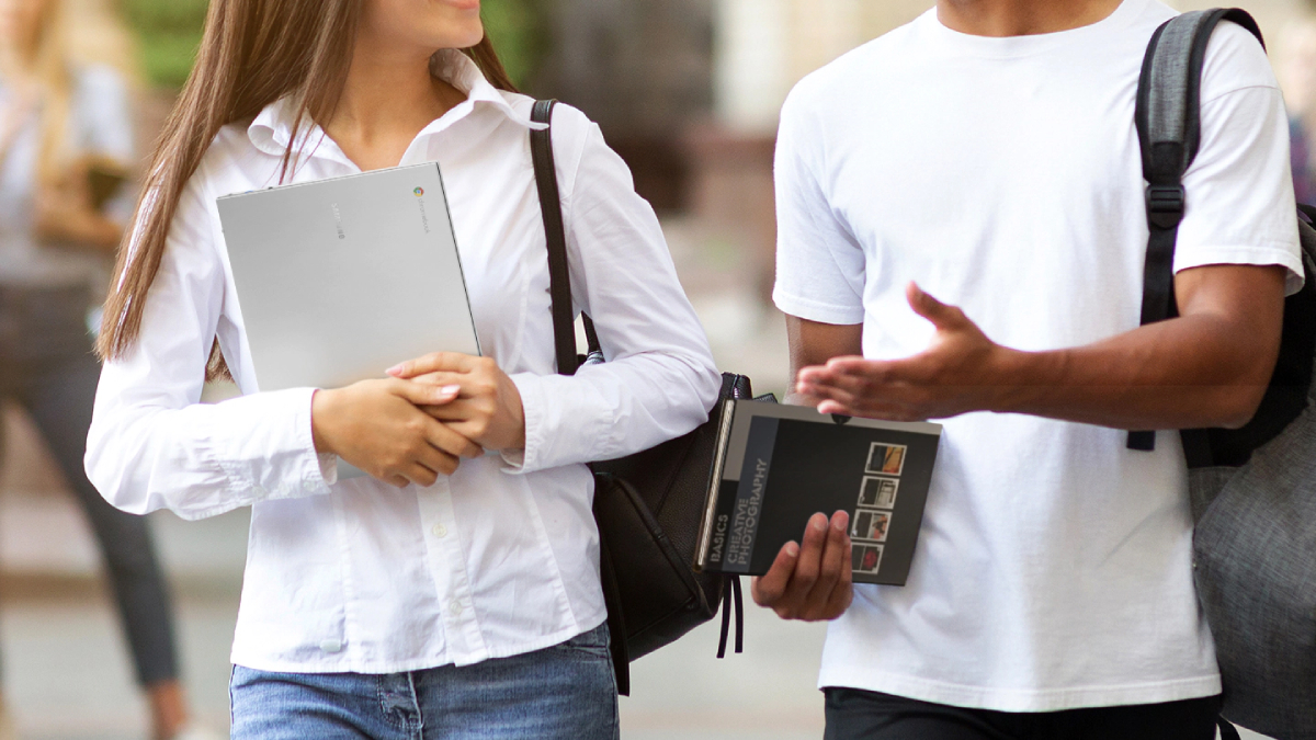 Dos personas en la calle; la mujer está sosteniendo una computadora portátil Samsung Chromebook Go.