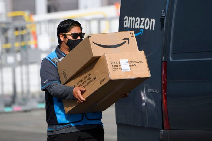 La imagen muestra a un trabajador de Amazon bajando unas cajas de un vehículo.