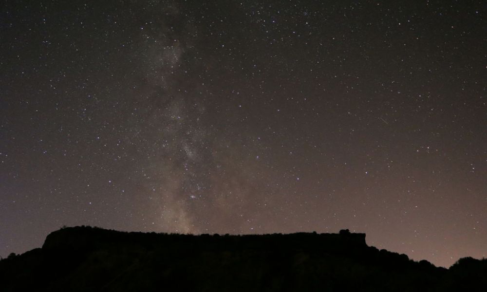 La imagen muestra una montaña y el cielo nocturno sobre un sector desértico.