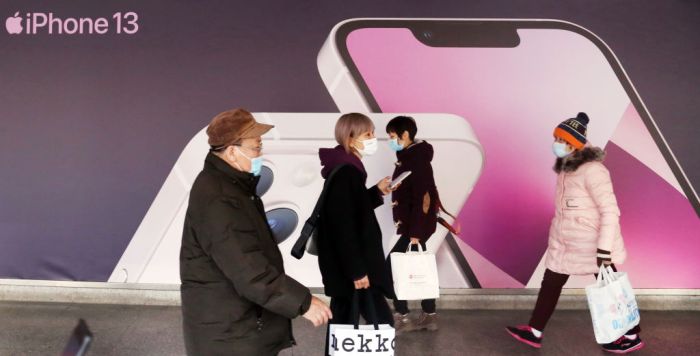 La imagen muestra un grupo de personas caminando frente a una publicidad del iPhone 13 en China.