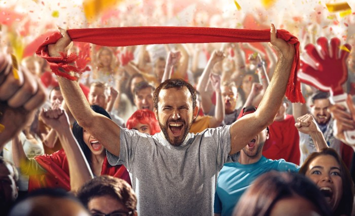 Un grupo de hinchas del fútbol en celebran en un estadio con una bufanda de color rojo