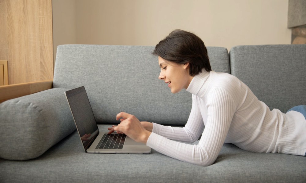 Una mujer usa una MacBook en un sofá.