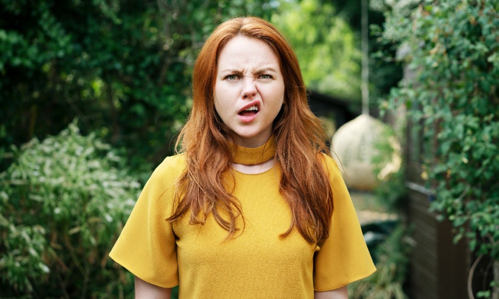 Una mujer colorina viste una polera amarilla con cara de pregunta