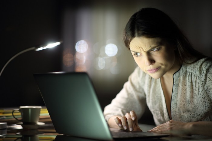 Mujer mira con escepticismo la pantalla de una computadora durante la noche.