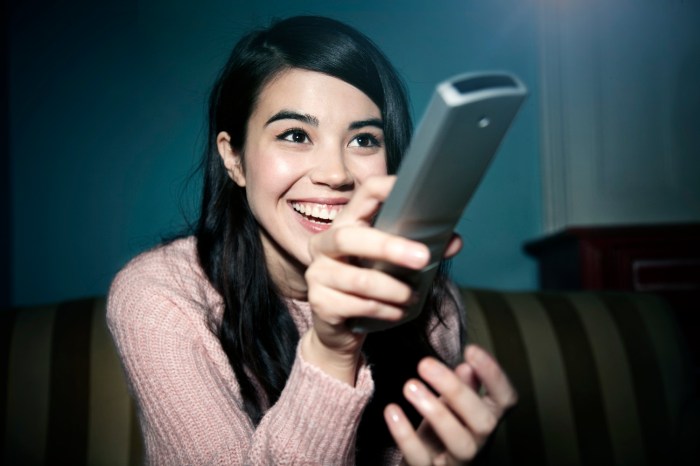 Una mujer sonríe mientras mira sostiene un control remoto y mira televisión