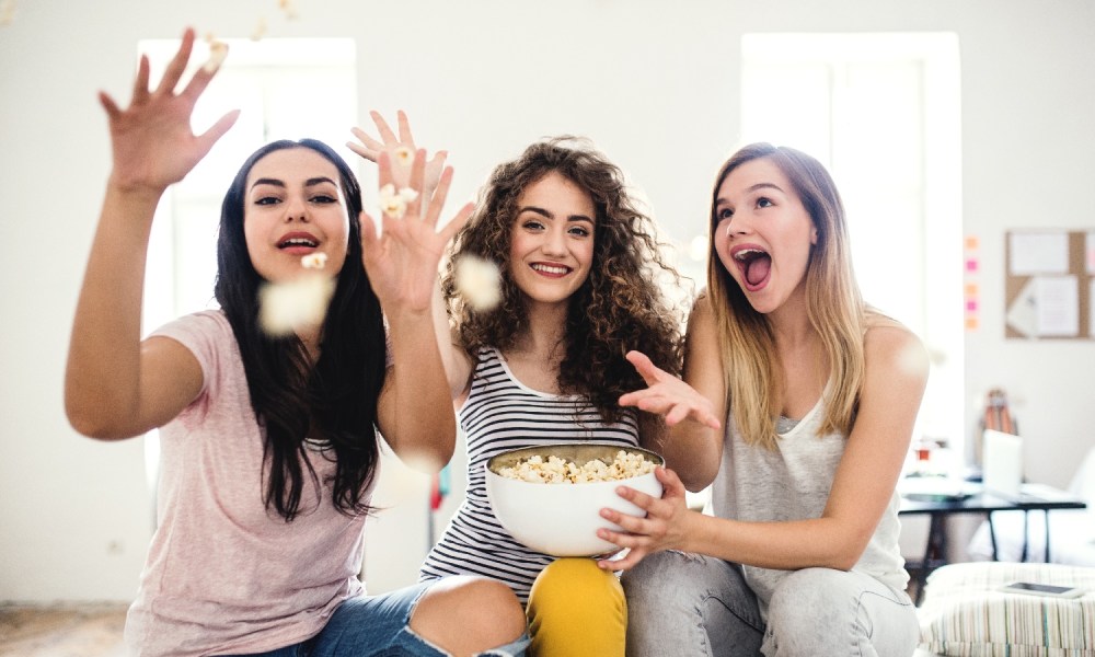 Tres mujeres ríen y disfrutan sentadas en un sillón mientras comen palomitas de maíz