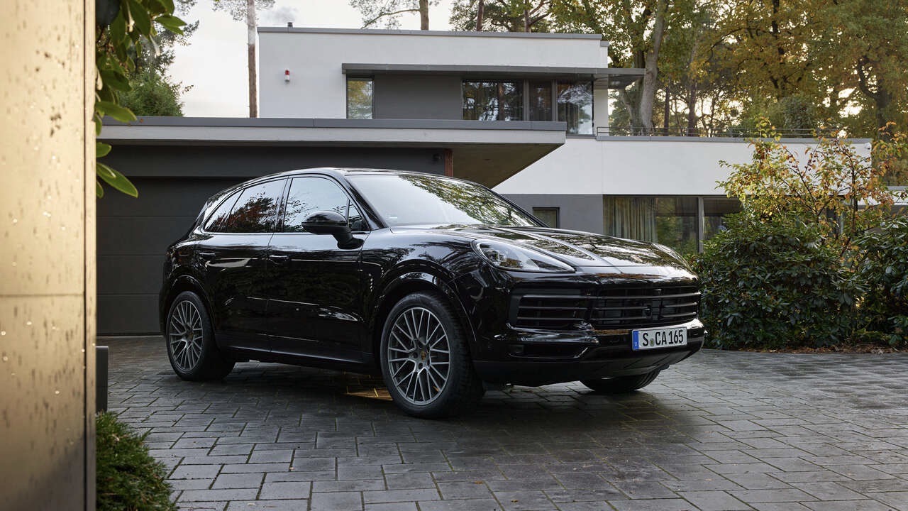 Vista frontal de dos cuartos de la Porsche Cayenne Platinum Edition 2022 en movimiento estacionada frente a una casa moderna.