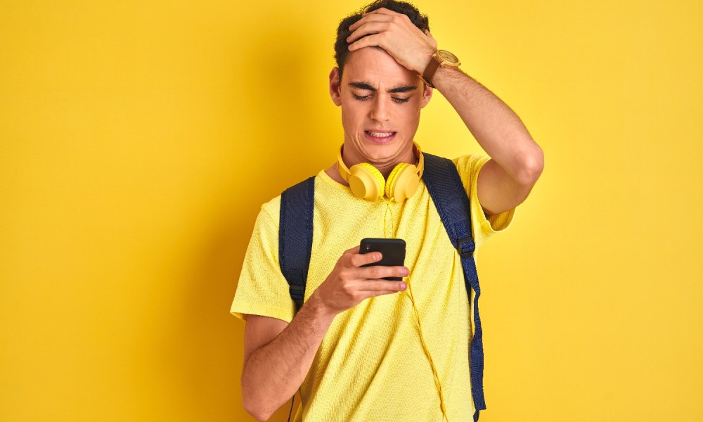 Un joven con camisa amarilla mira con cara de preocupación su teléfono