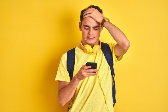 Un joven con camisa amarilla mira con cara de preocupación su teléfono