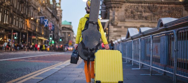 Un músico camina con una maleta amarilla y una guitarra en su espalda