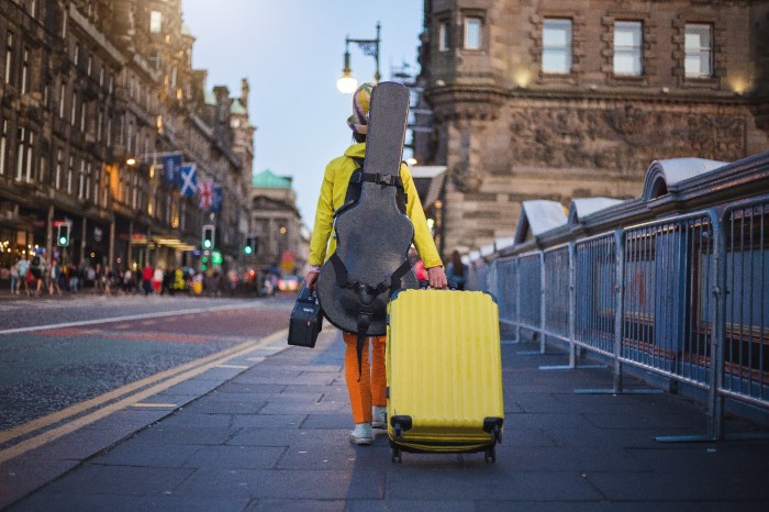 Un músico camina con una maleta amarilla y una guitarra en su espalda
