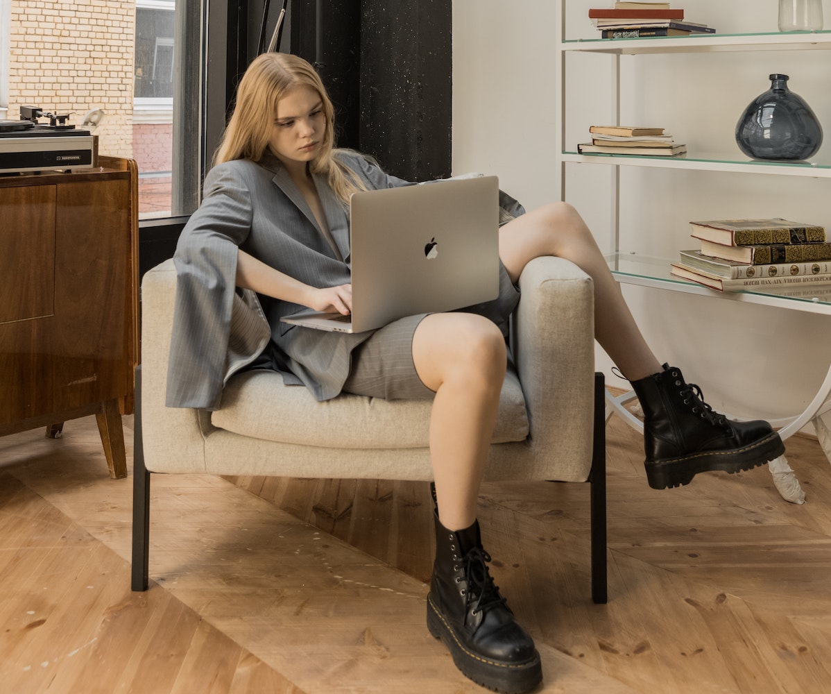 Muchacha joven echada en un sillón con una laptop Mac.