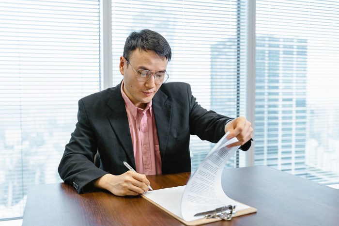 Un hombre de ropa formal en una oficina lee un documento antes de firmarlo.