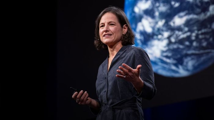 Persona dando una charla TED; en el fondo se ve una imagen del planeta.