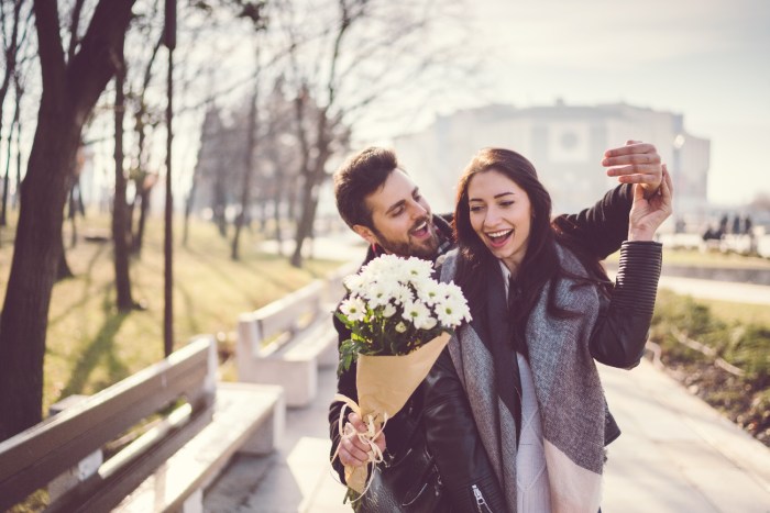 Un hombre sorprende con flores a una mujer mientras caminan por un parque
