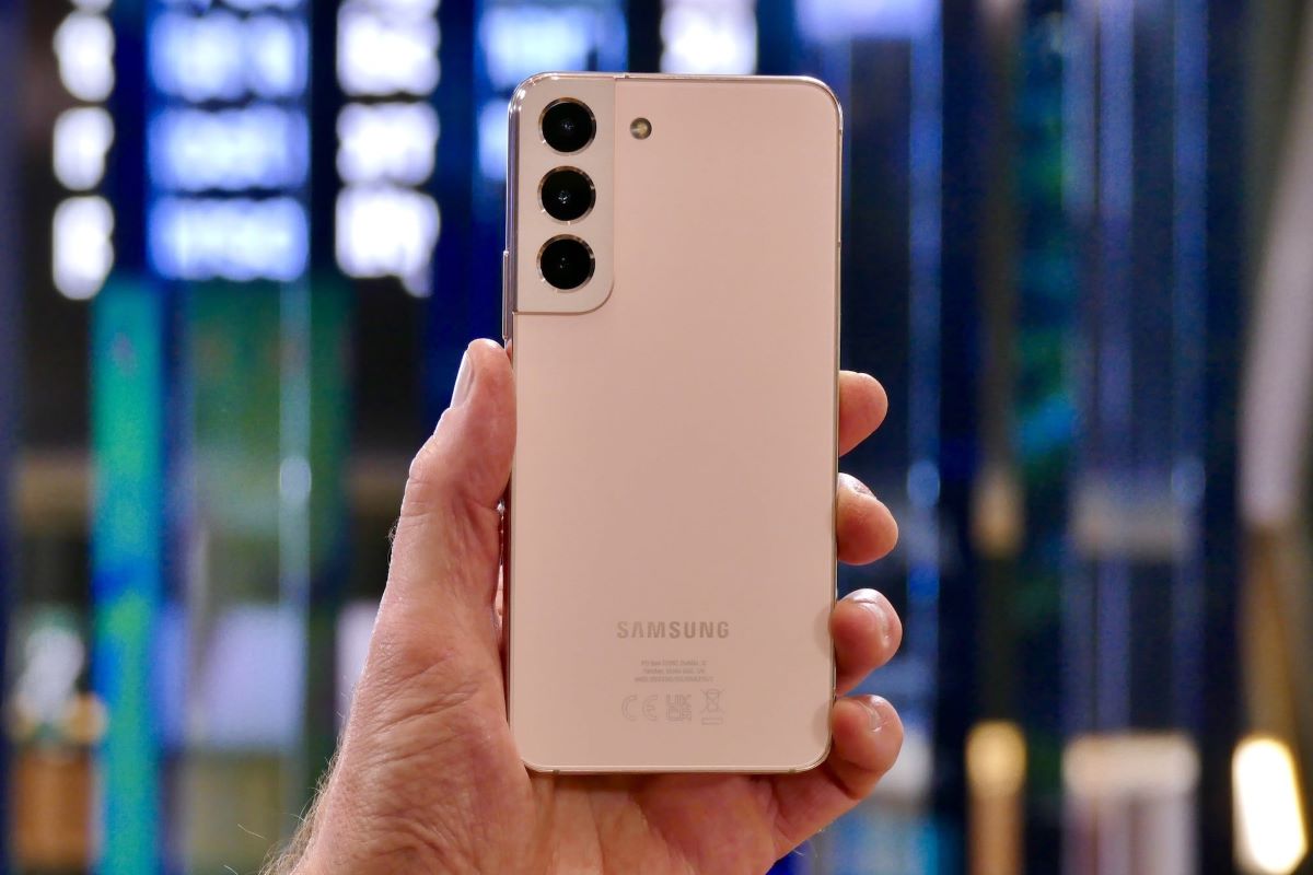 Galaxy S22 en color oro rosa en la mano de una persona mostrando la parte posterior.