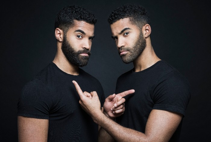 Dos gemelos con barba y polera negra se apuntan mutuamente