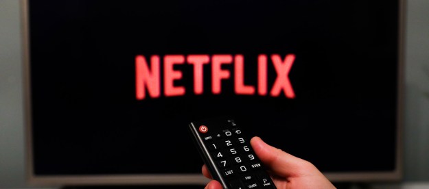 Un televisor muestra el logo de Netflix mientras una mano apunta con un control remoto.