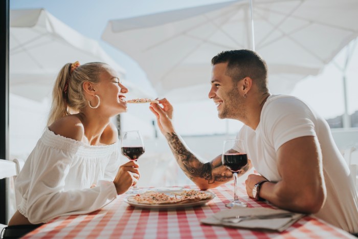 Una mujer y un hombre sonríen mientras comen pizza en una mesa con mantel cuadriculado