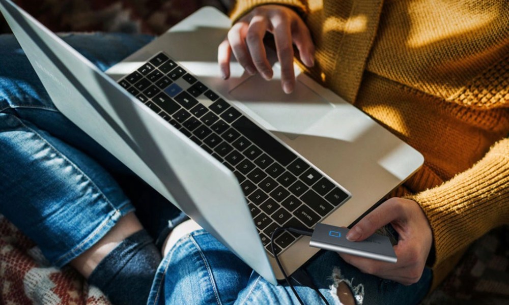 Una chica sentada con una laptop en sus piernas y conectado una unidad SSD Samsung T7.