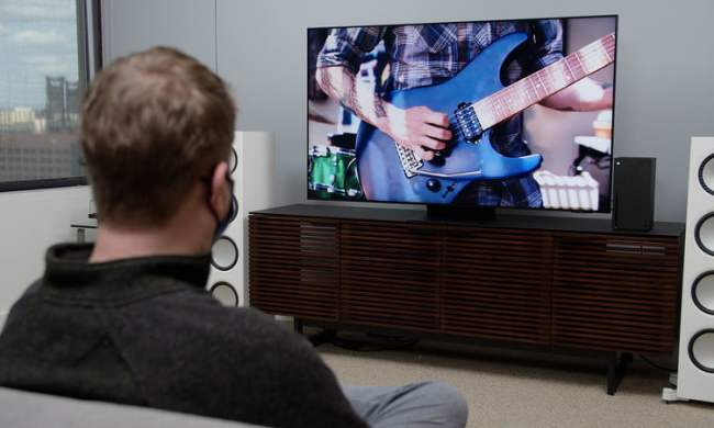 Un hombre ve a una persona tocar la guitarra eléctrica en televisión.