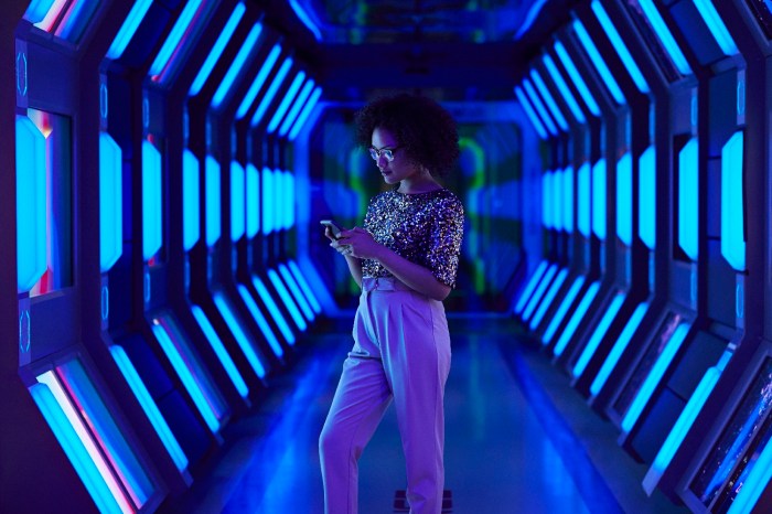 Una mujer revisa un teléfono inteligente en un pasillo con pantallas y luces led