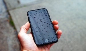 Una mano sostiene un teléfono celular mojado bajo la lluvia.