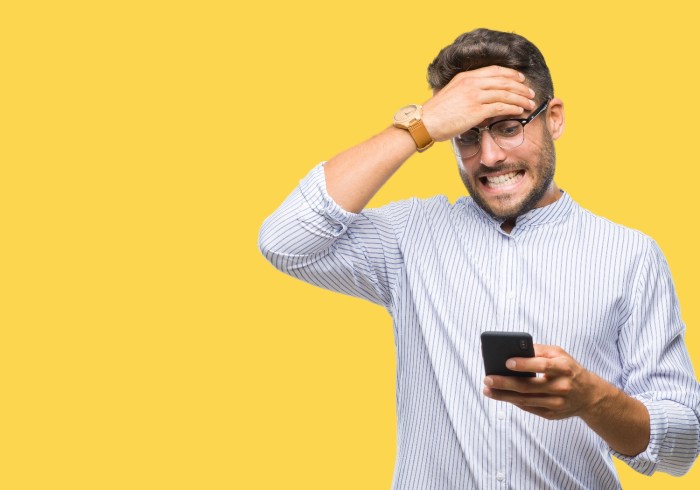Un hombre mira con cara de preocupación su teléfono con una pared amarilla en el fondo.