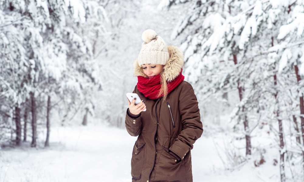 Una mujer sostiene un teléfono en un bosque con nieve