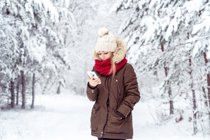 Una mujer sostiene un teléfono en un bosque con nieve