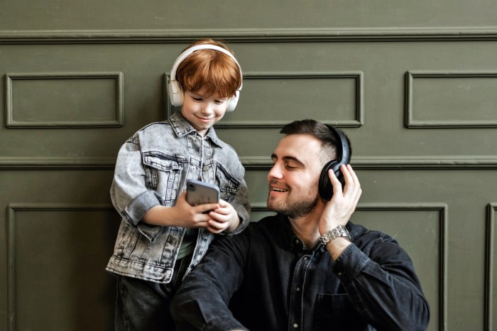 Un hombre y un niño escuchan música de un celular con audífonos.