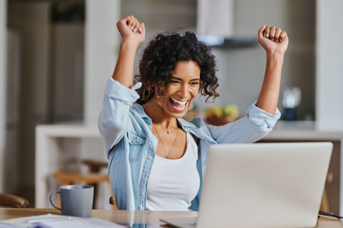 Una mujer levanta sus brazos en señal de celebración mientras trabaja en su computadora