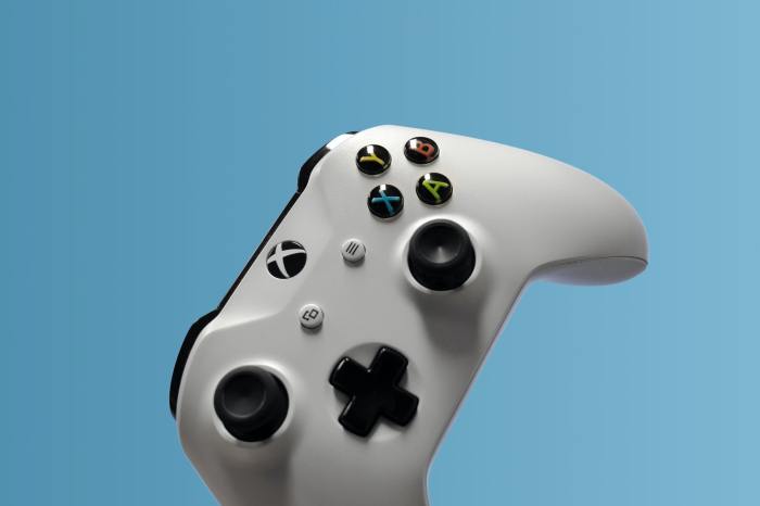 Un control de Xbox One color blanco sobre un fondo azul claro.