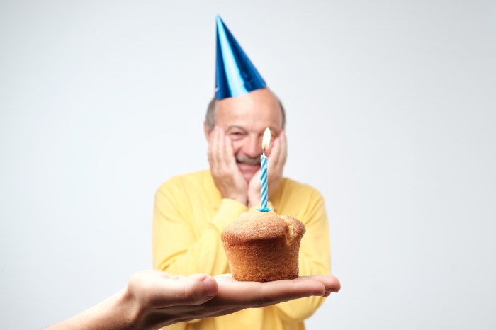 Una persona sostiene un queque con una vela para celebrar el cumpleaños de un hombre con gorro azul