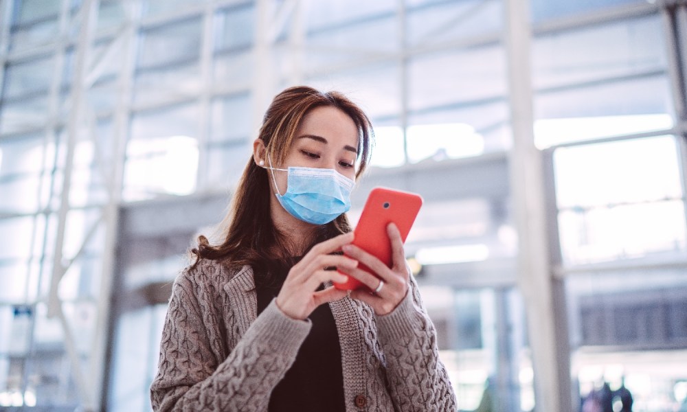 Una mujer usa su teléfono con mascarilla