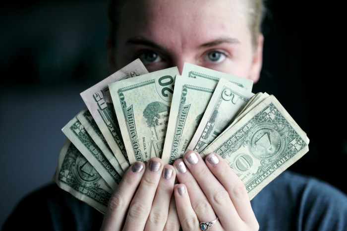 Una chica asoma sus ojos detrás de un abanico de dólares que sistiene frente a su rostro.