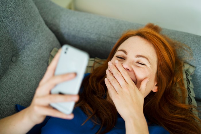 Una mujer ser ríe mientras observa su celular.