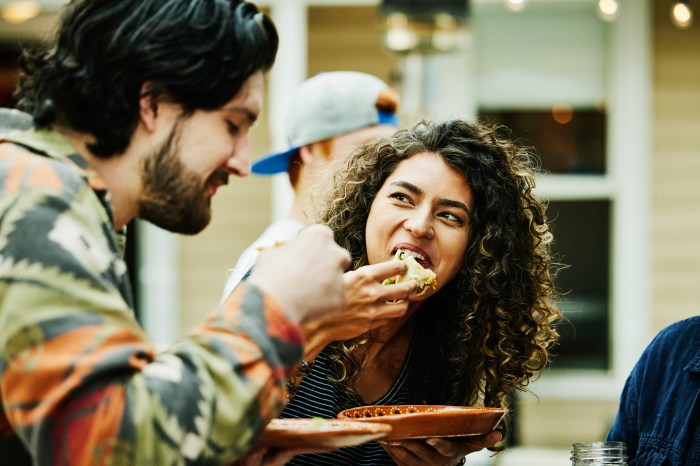 Una pareja de jóvenes mientras come tacos sobre unos platos.