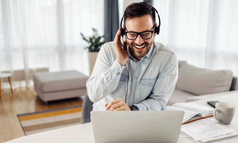 Un hombre joven con barba y lentes contesta una llamada en su computadora