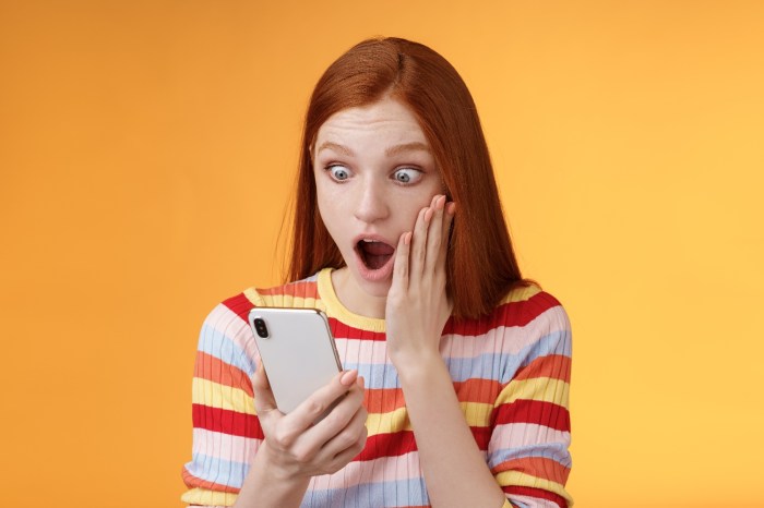 Una mujer colorina mira su teléfono con cara de sorpresa 