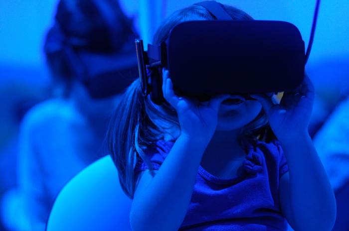 Una niña utiliza un visor de realidad virtual. Toda la foto es azul.