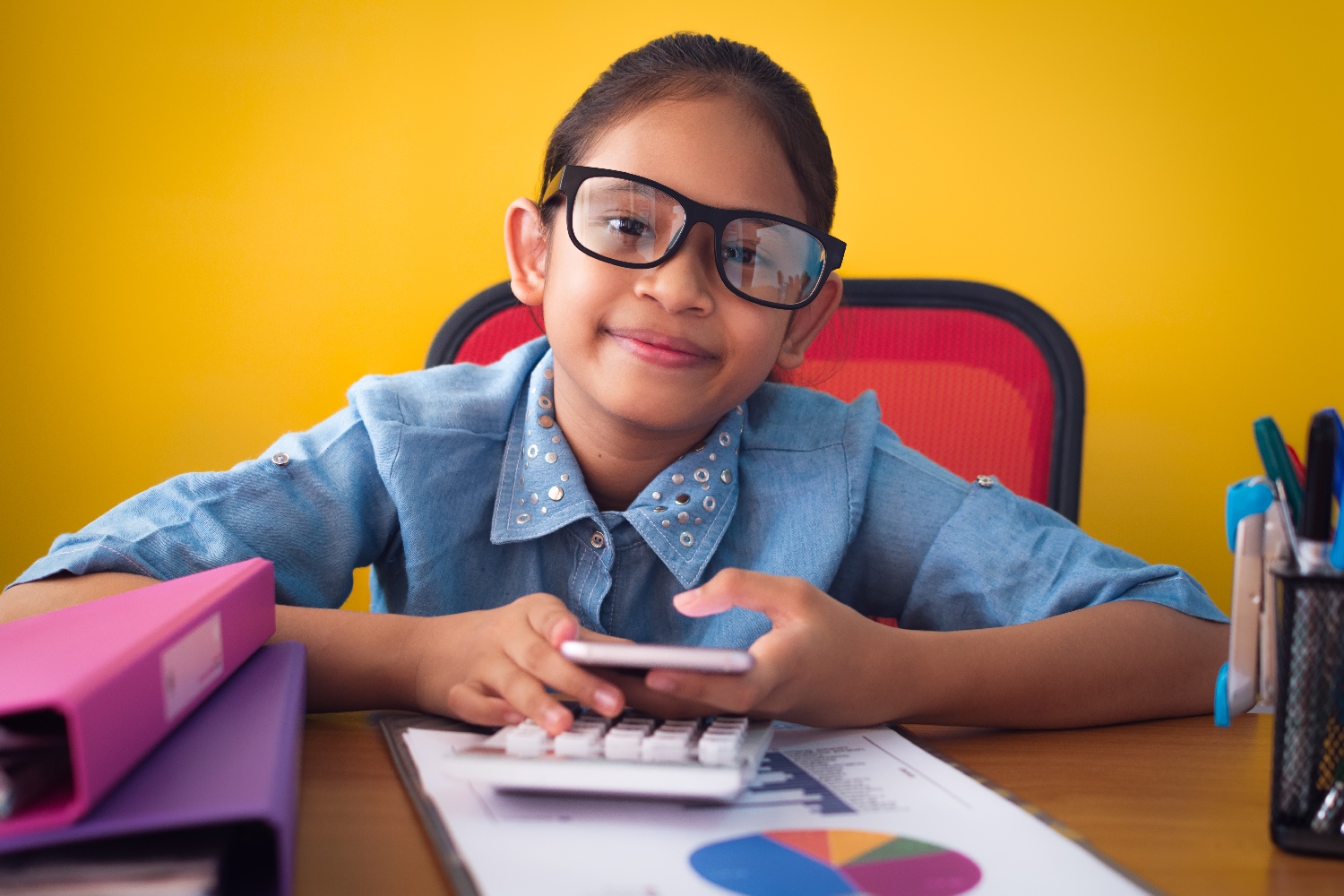 Una niña estudia sentada en un escritorio mientras sostiene un teléfono