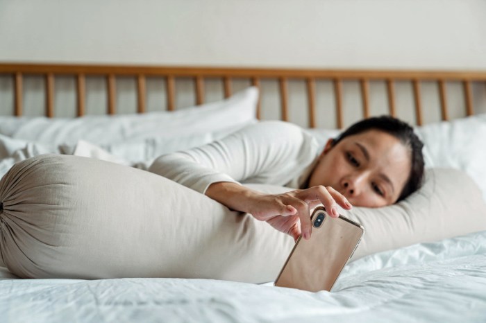 Una mujer recostada en su cama mira con melancolía la pantalla de su celular.