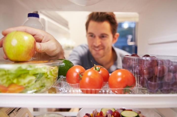 Un hombre toma una manzana en el interior de un refrigerador.
