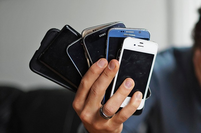 Una mano sostiene un montón de teléfonos celulares viejos.