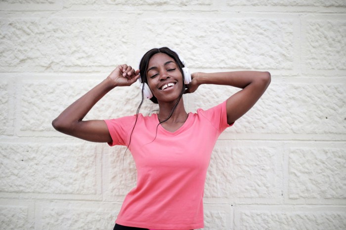 Una chica disfruta música con audífonos frente a un muro blanco.