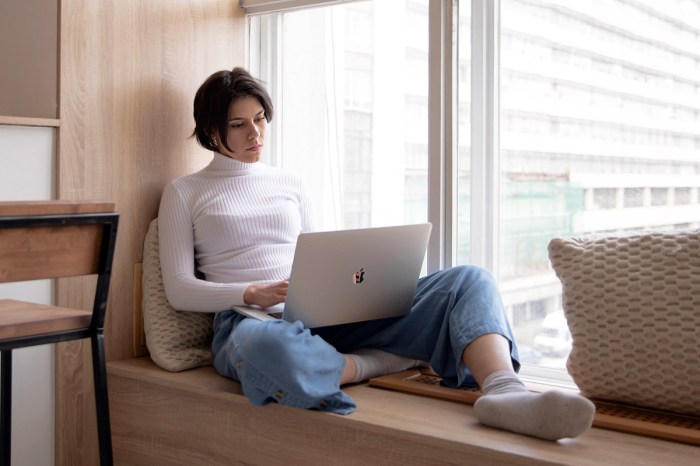 Una mujer trabaja concentrada en una laptop MacBook sentada junto a una ventana.