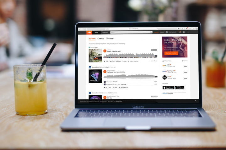 Una laptop en la que se ve la página de Soundcloud en una mesa junto a un jugo de naranja.