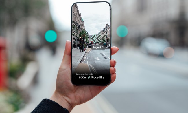 Over the shoulder view of young woman locating direction with augmented reality technology on smartphone on city street. Hand holding smartphone using an GPS application to show the way by virtual arrow. Mockup image for woman using smartphone.