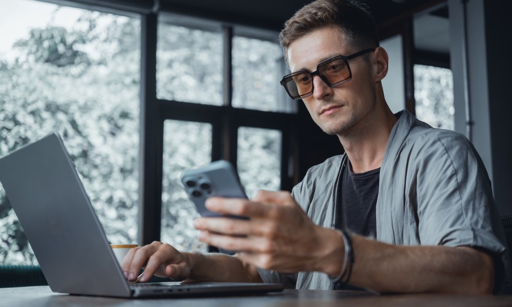 Hombre con una laptop y un iPhone – Cómo liberar un iPhone para usarlo en otros operadores.